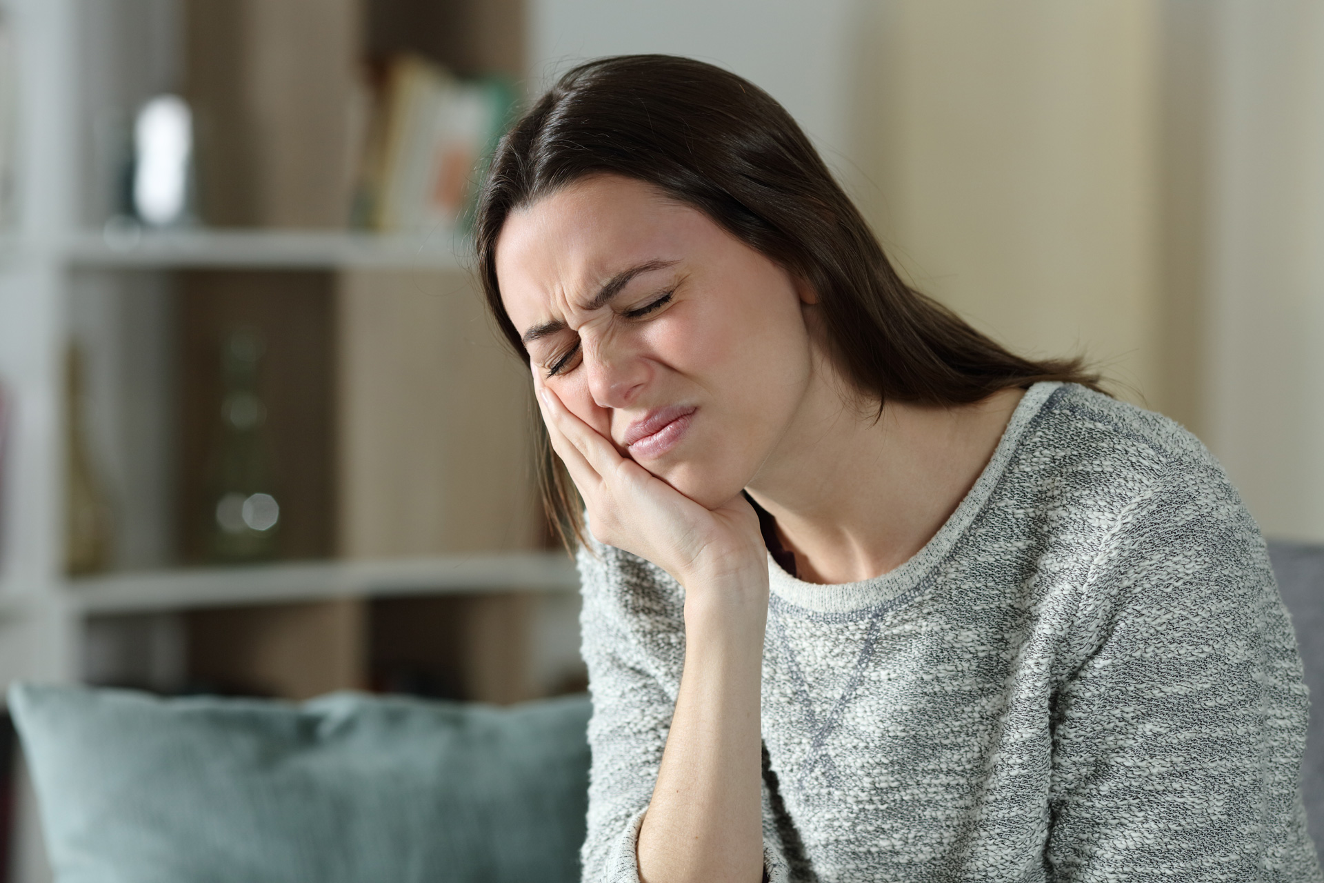 A woman in pain holding her jaw with one hand.