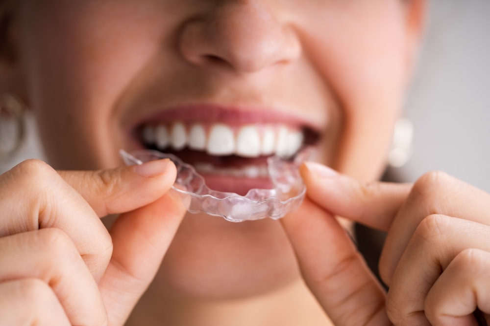 A woman smiling while holding an Invisalign aligner obtained from orthodontic treatment.