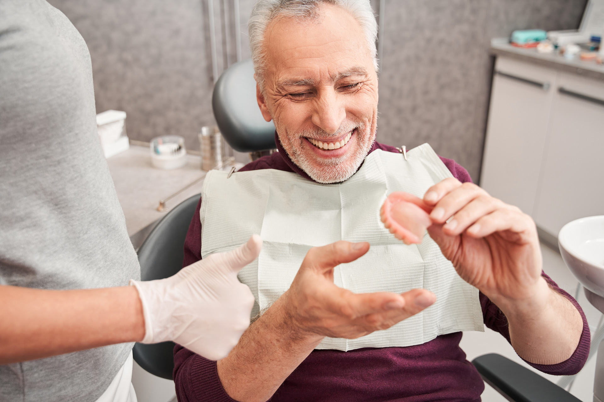 A man smiles while holding his dentures.