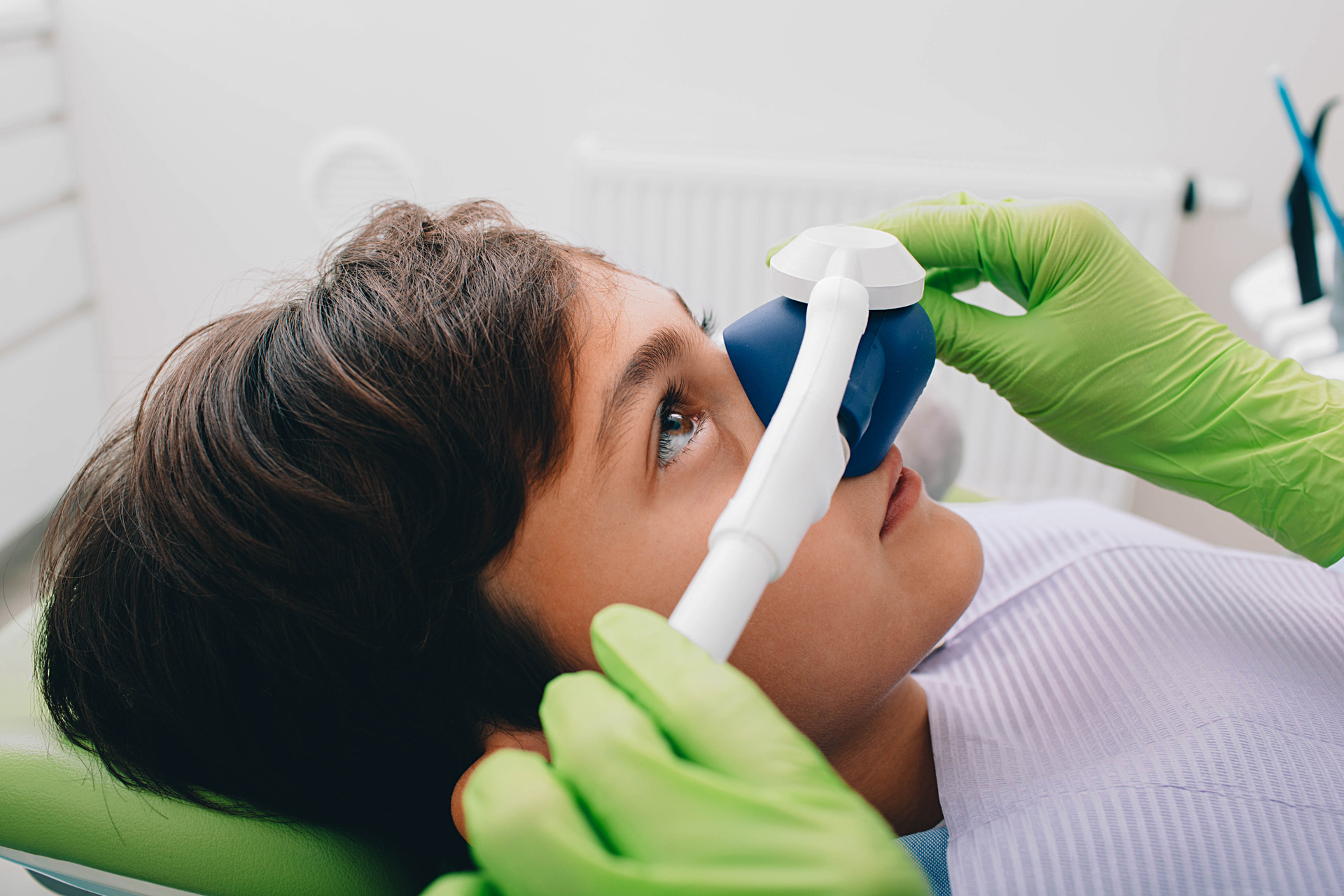 A young patient receiving nitrous oxide sedation through a nasal mask in a dental chair