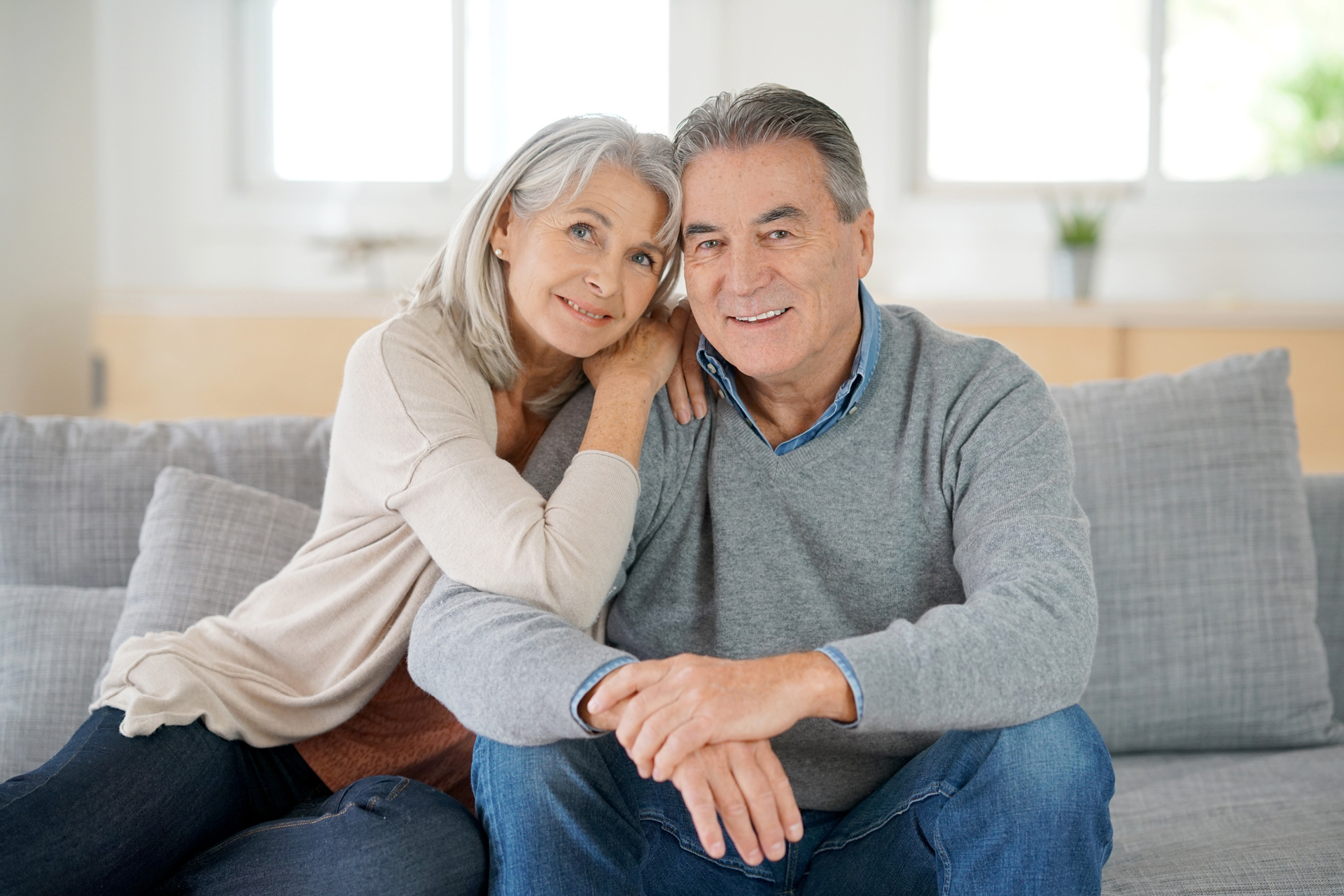 An older couple with bright smiles relaxing on a couch, embodying love and happiness in their shared moment.