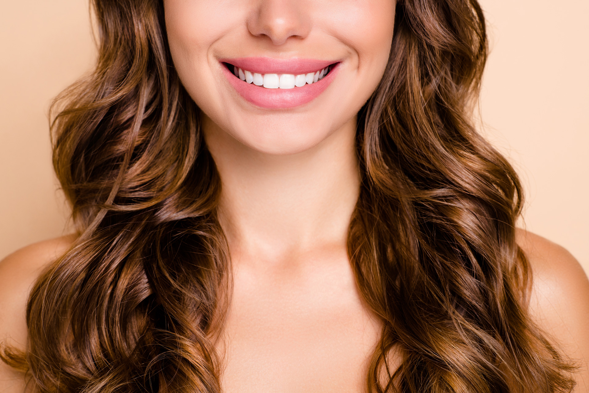 A woman with long, wavy hair and bright white teeth smiles warmly.