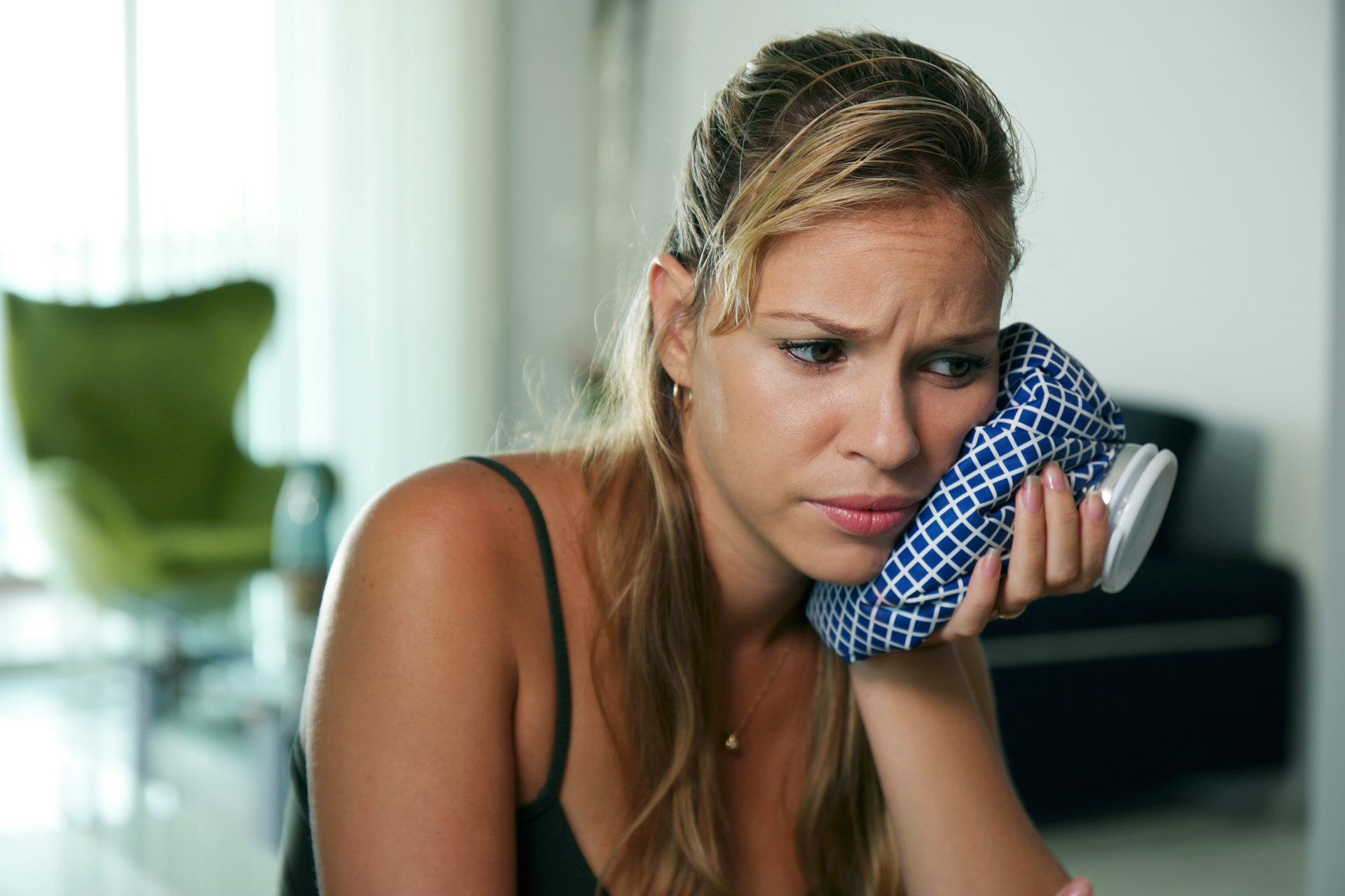 A woman in pain holding an ice pack to her jaw after a tooth extraction.