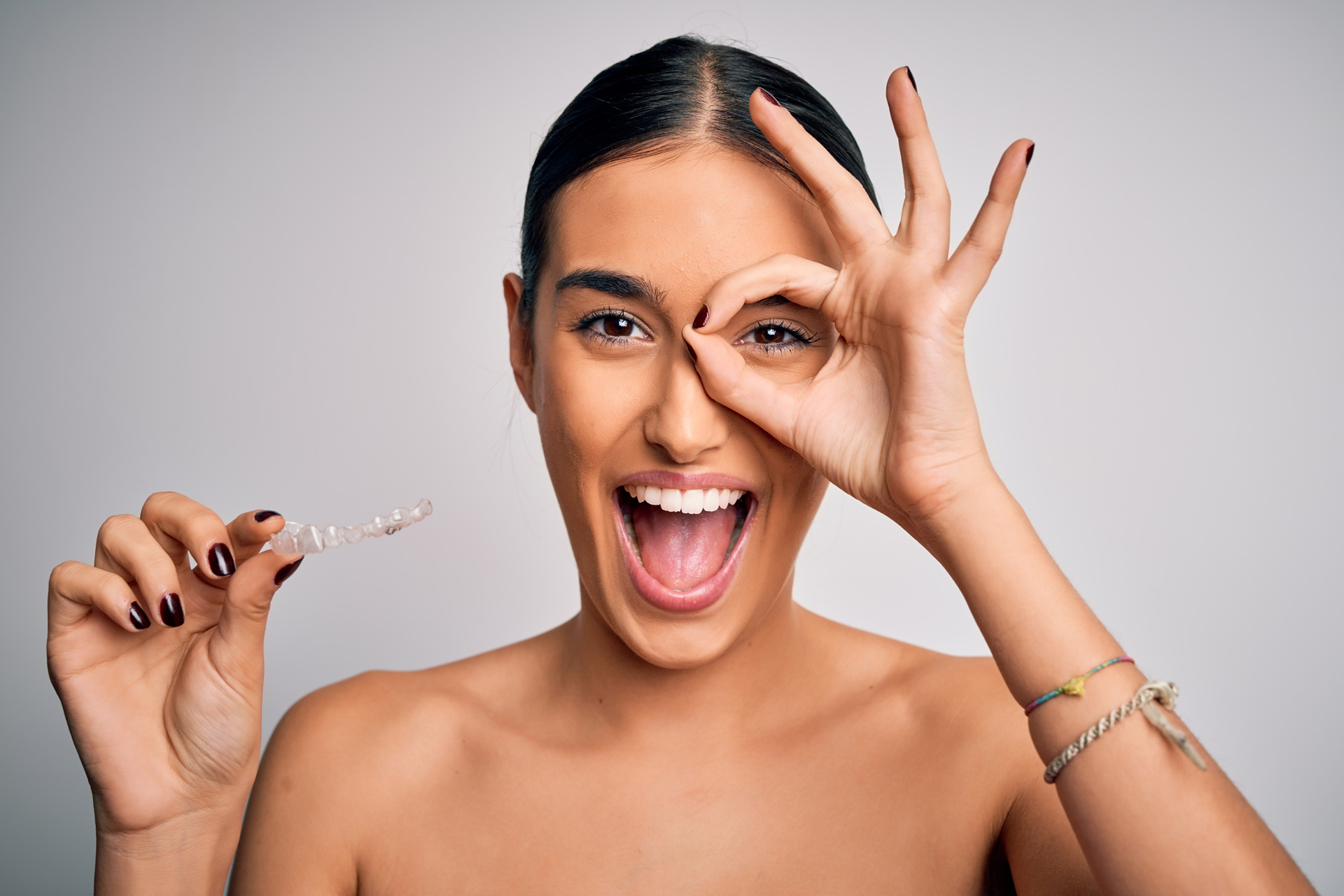 A woman holds her Invisalign retainer up while smiling.